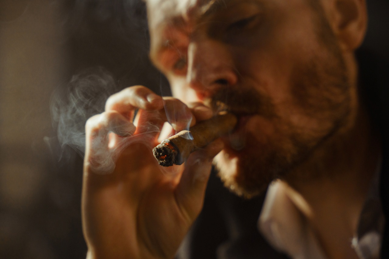 Close up of a male face with a blond beard, smoking a cigar in a beautiful light